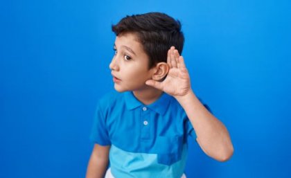 Young boy with his left hand cupped to his left ear.